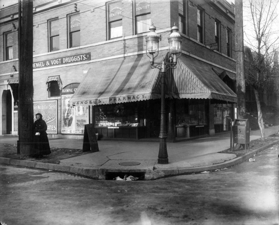 The Mengel & Vogt pharmacy at Taylor and Page Avenues, 1900. A woman is standing next to a pole in front of the building. The building still exists and appears to be vacant.