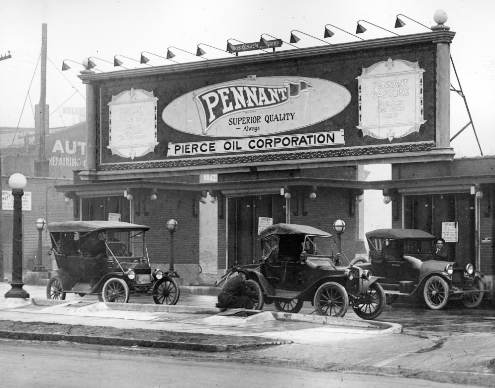 Pennant Pierce Oil Corporation filling station, 1900. Three cars are visible in front. A man appears to be putting air into the tire of one of the cars.