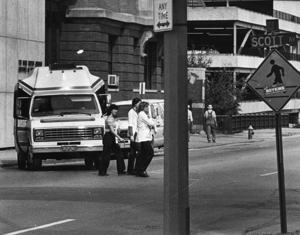 Pedestrians trying to cross Euclid Ave with a van on their tails thats making a left turn from Euclid into Scott, 1982