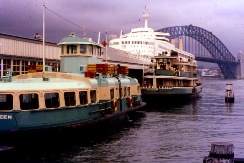 The harbour ferries Kooleen and Kameruka in the foreground with an unknown ocean liner, probably the P&O Canberra, and the harbour bridge behind, Circular Quay, Sydney, 1969