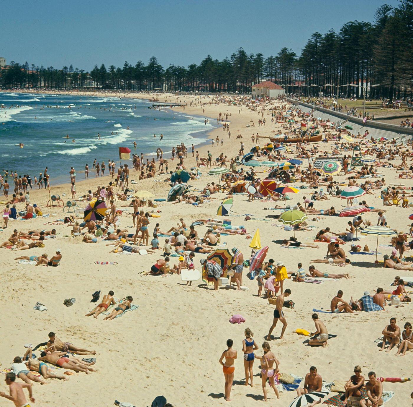 Visitors sunbathe under umbrellas on the sandy beach facing the Pacific Ocean in the suburb of Manly in northern Sydney, 1965