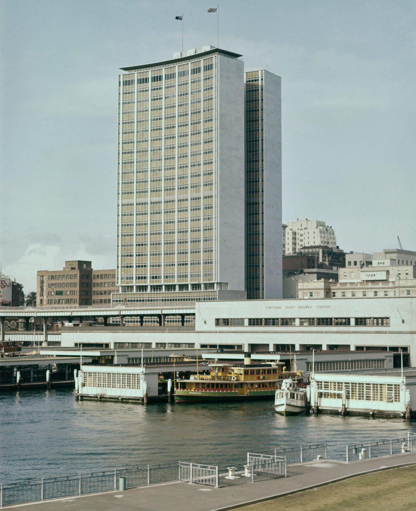 A ferry docked at the Circular Quay Railway Station passenger terminal underneath the AMP Building office block in downtown Sydney, 1963