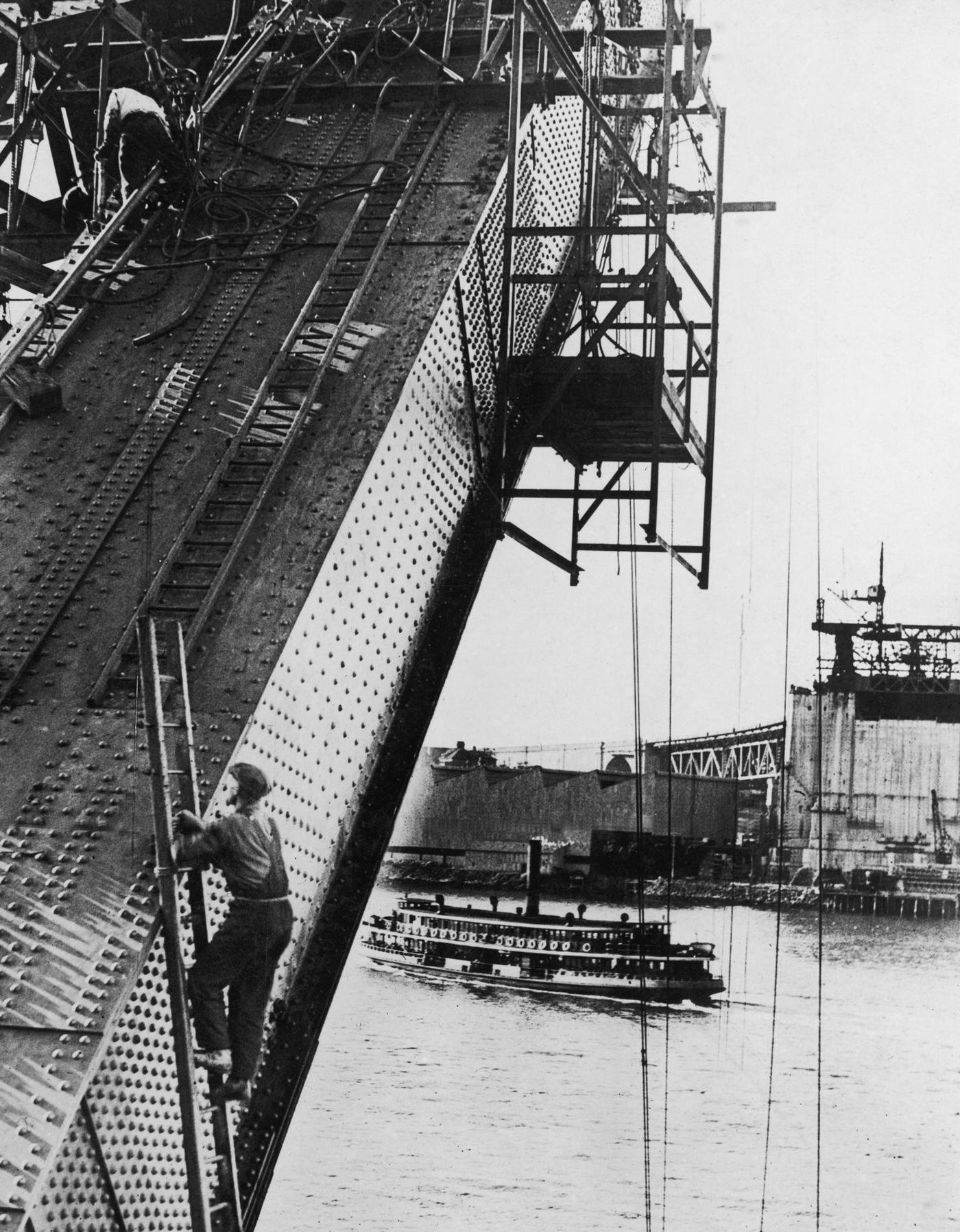 A passenger steamer passes under Sydney Harbour Bridge during the construction of its arch, 1930.