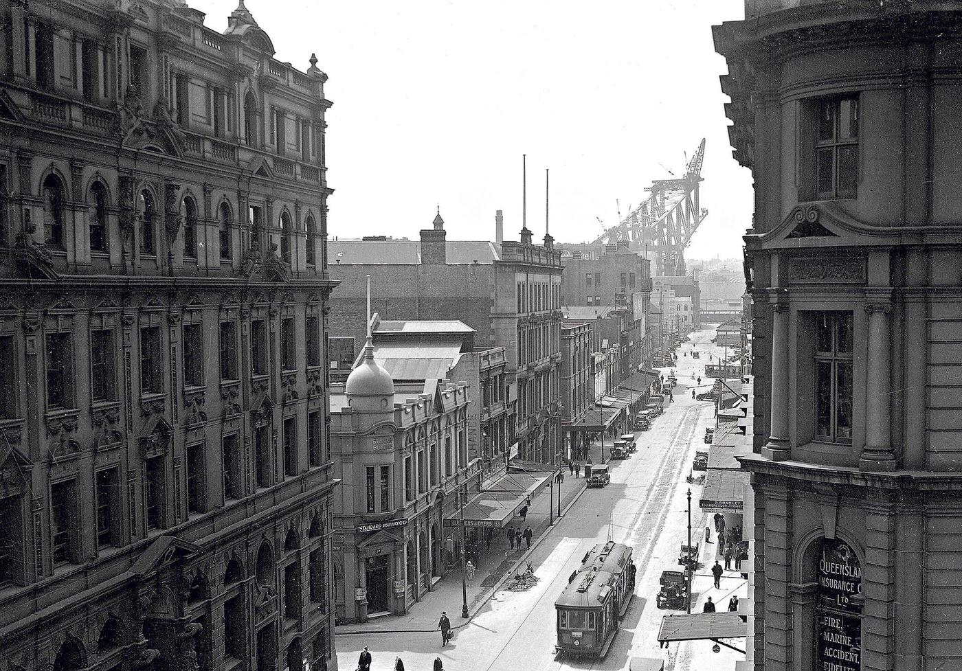 Pitt Street, Sydney in the 1920s with construction of the Sydney Harbor Bridge in the background.