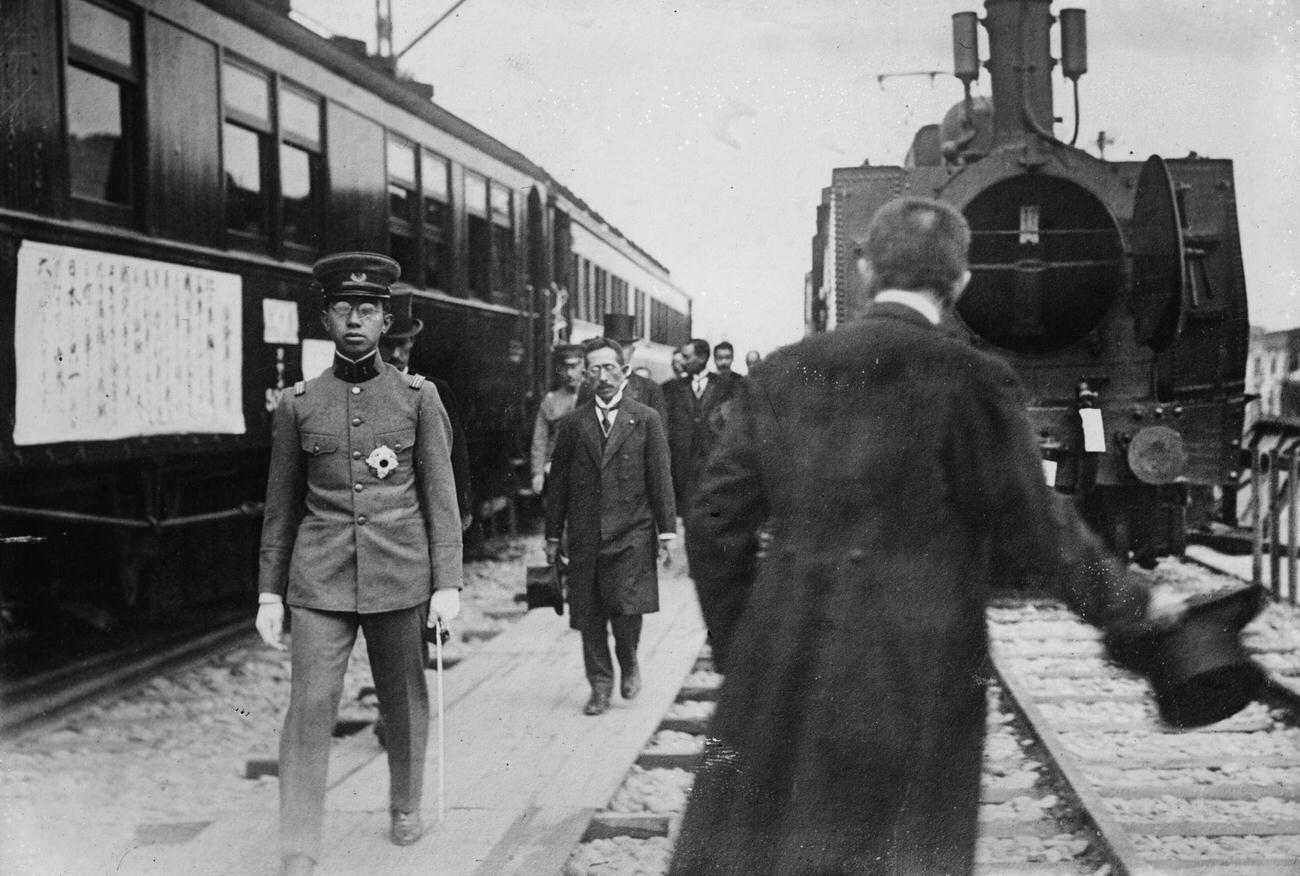 Crown Prince Hirohito, in uniform walks beside a train at station, 1900
