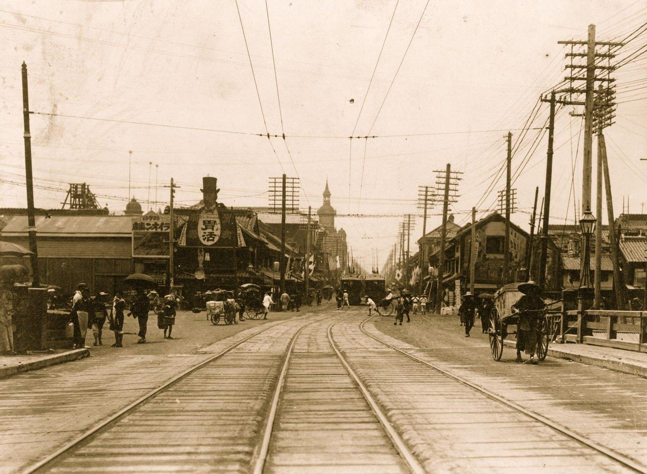 Center of Tokyo street with cable car tracks in foreground, buildings and people in background, 1905