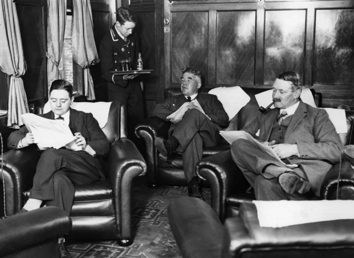 Gentlemen relax in leather armchairs on the Royal Scot, a train on the London, Midland and Scottish Railway, 1928.
