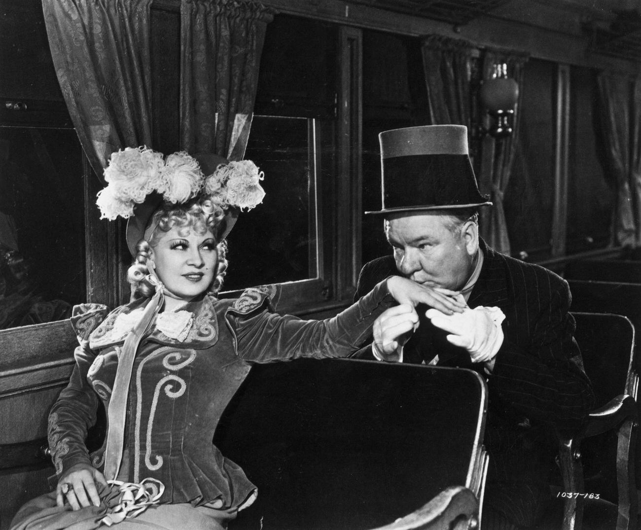 W C Fields kisses the hand of American writer, actor and comedian Mae West (1893 - 1980) while sitting aboard a train