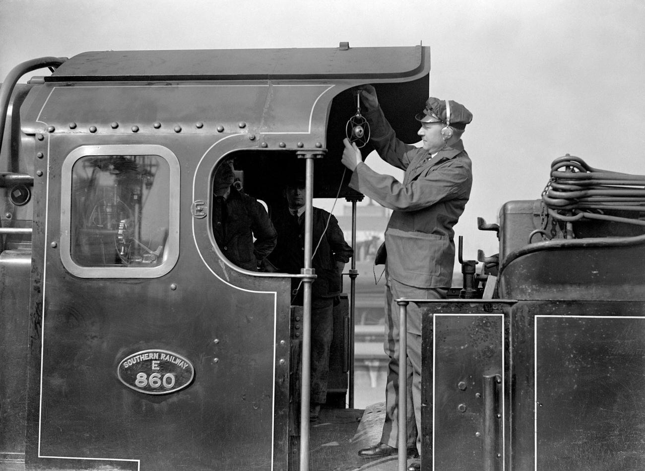 Reginald Foort traveling on the foot plate where he is seen adjusting the microphone, in an endeavour to secure local colour and time sound of which he will bemaking a gramaphone record of the popular "Choo Choo" train effects foxtrot.