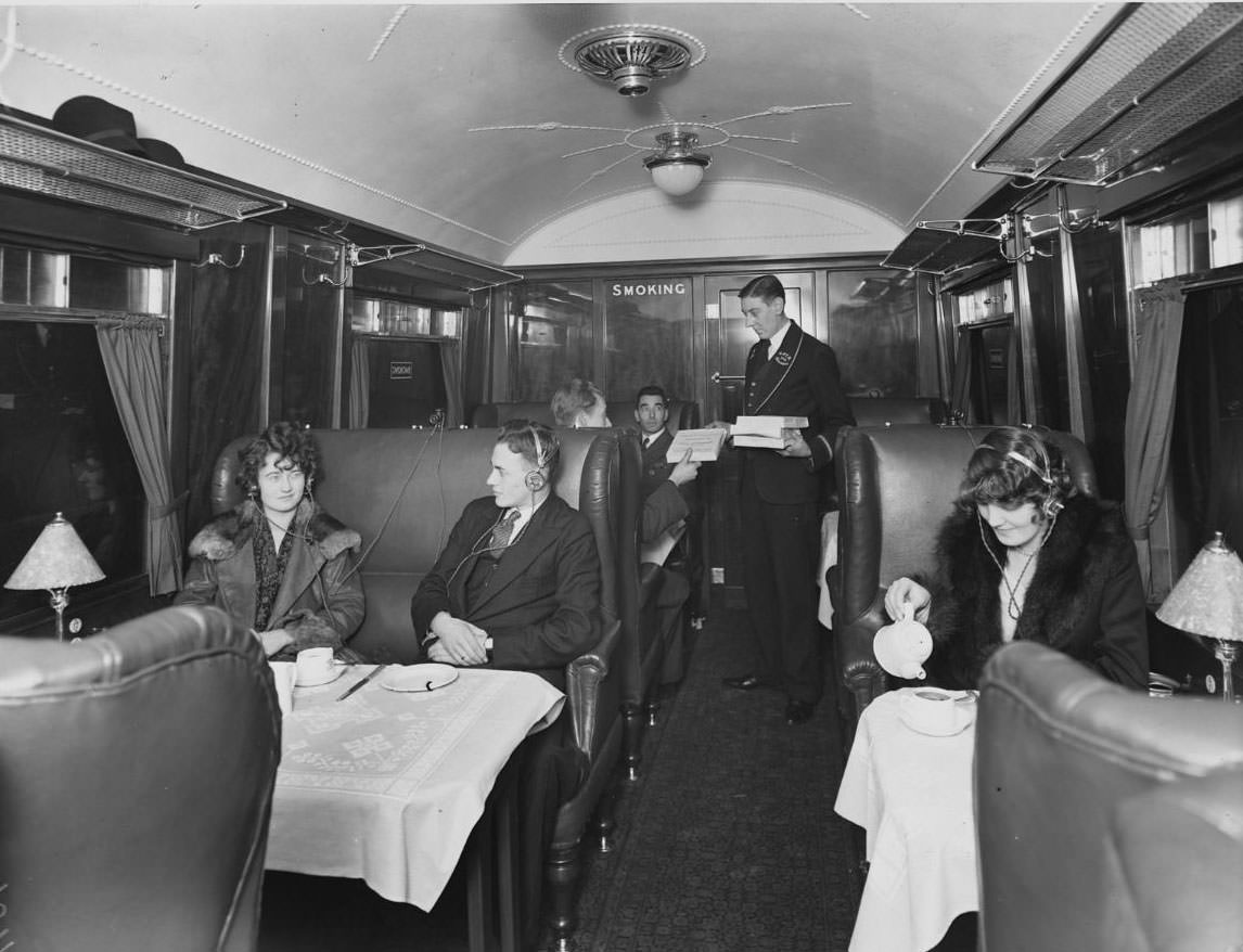 Rail passengers listening to the radio through personal headphones in the dining car of a train, 1930.