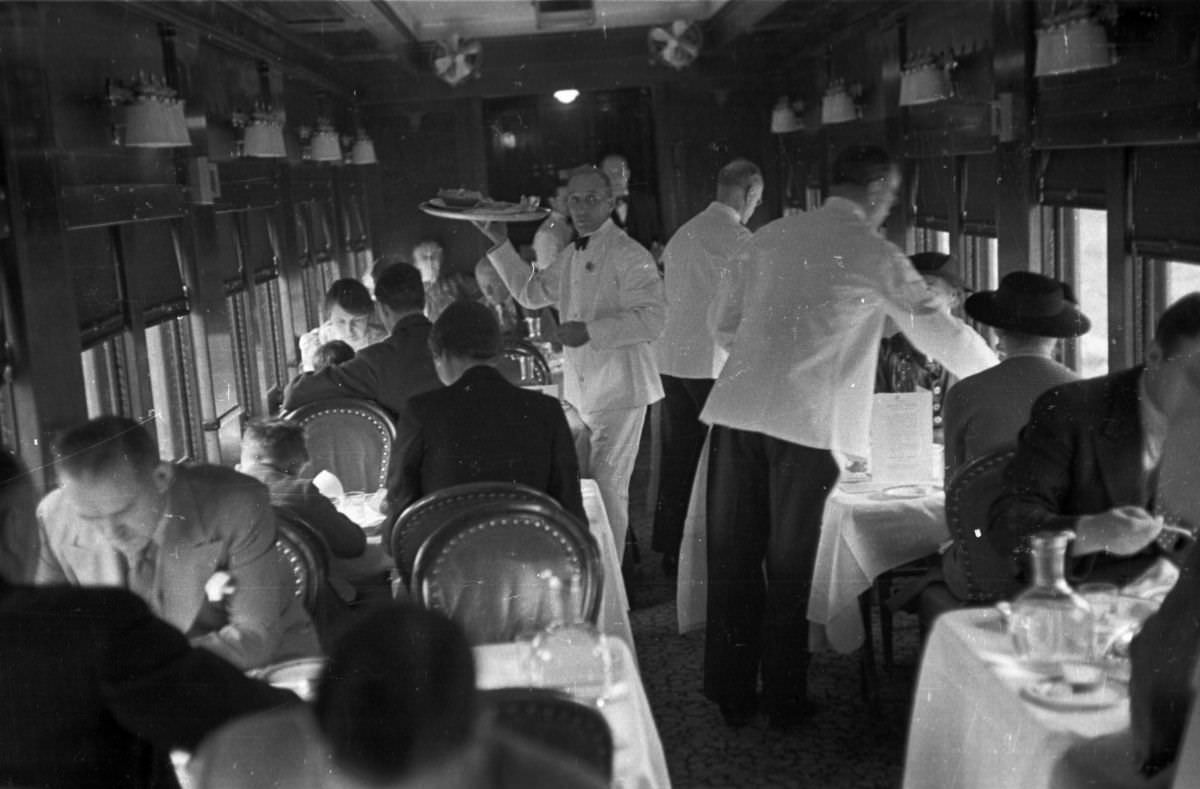 Waiters bringing food to passengers in the dining car of a Canadian Pacific Railway train during a three day journey across the country, 1939.