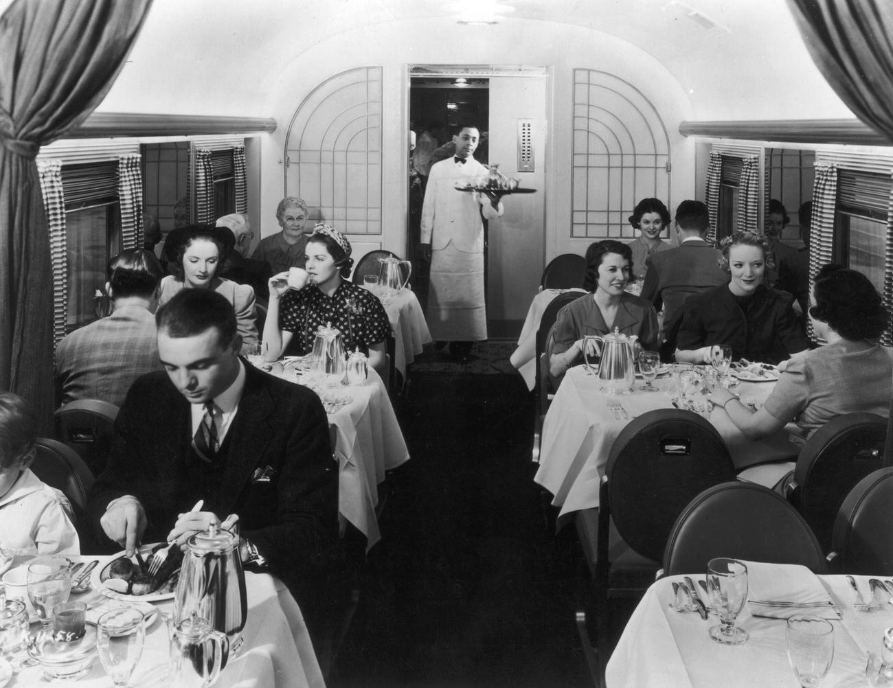 Express Restaurant. Interior view of a dining car on a train, with patrons seated at tables and a waiter holding a tray at the rear of the room, 1945