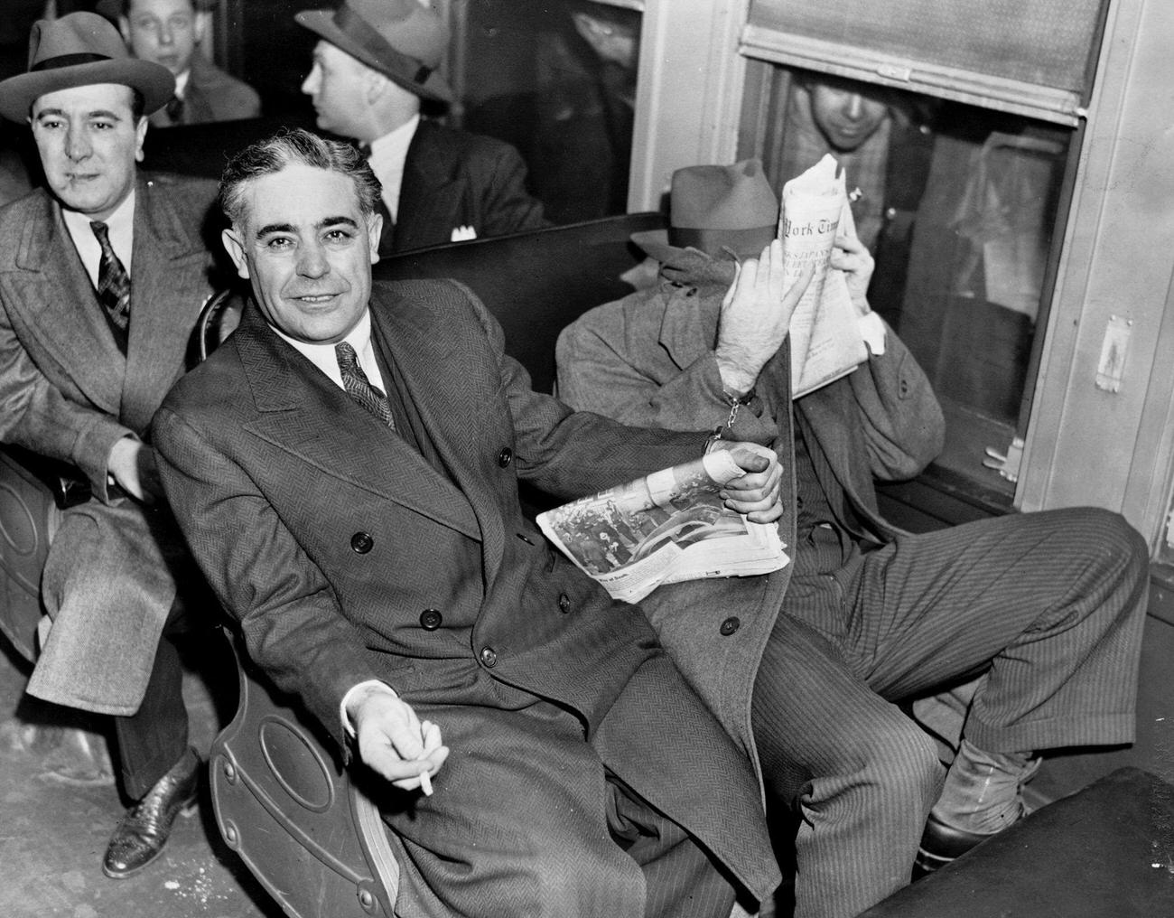 Surrounded by deputy sheriffs and shackled together, Emanuel (Mendy) Weiss, covering his face, and Louis Capone sit on the train en route to Sing Sing prison.