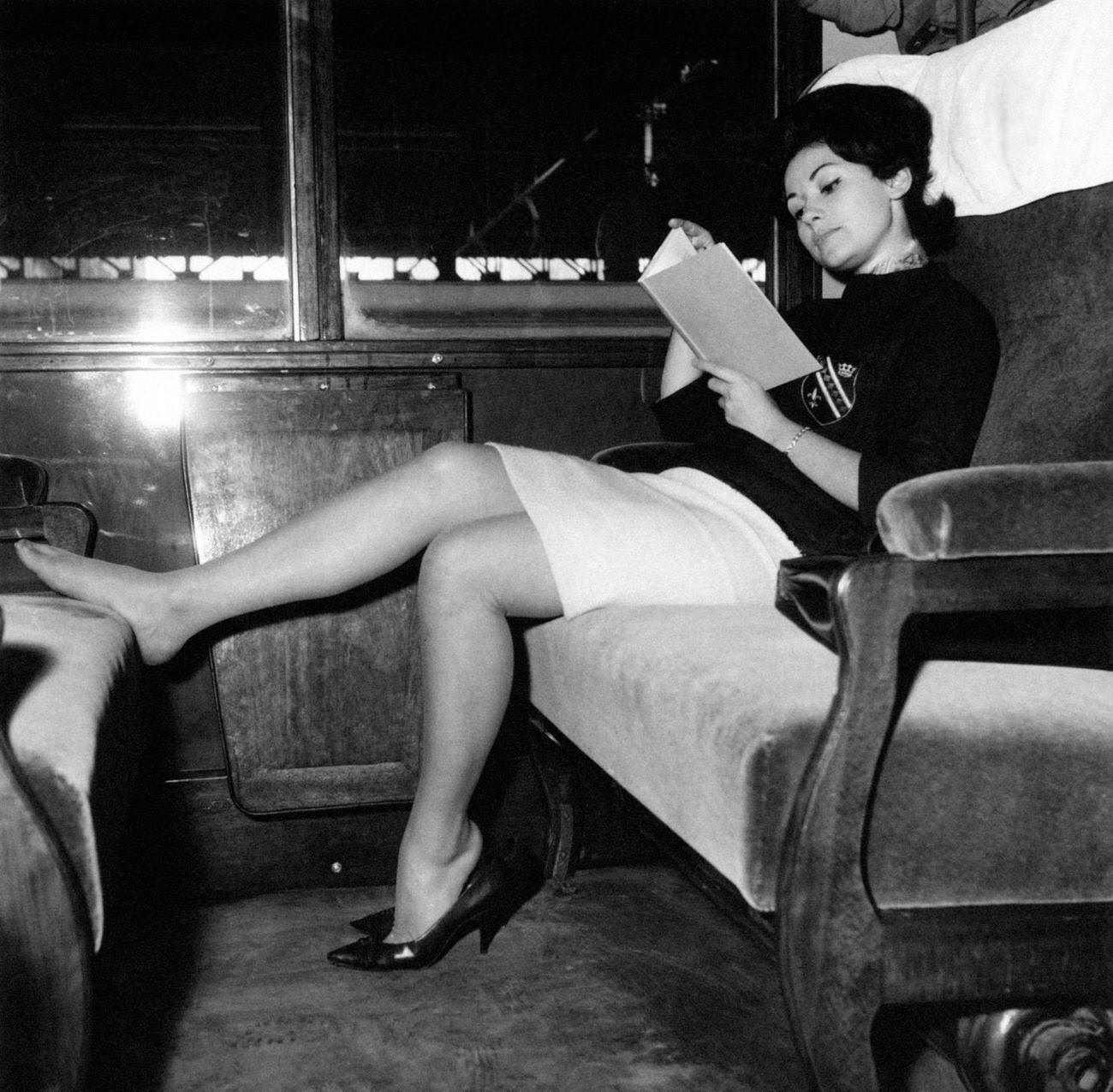 Italian miss Giuliana Copreni reading a book in a train carriage resting her feet on the seat.