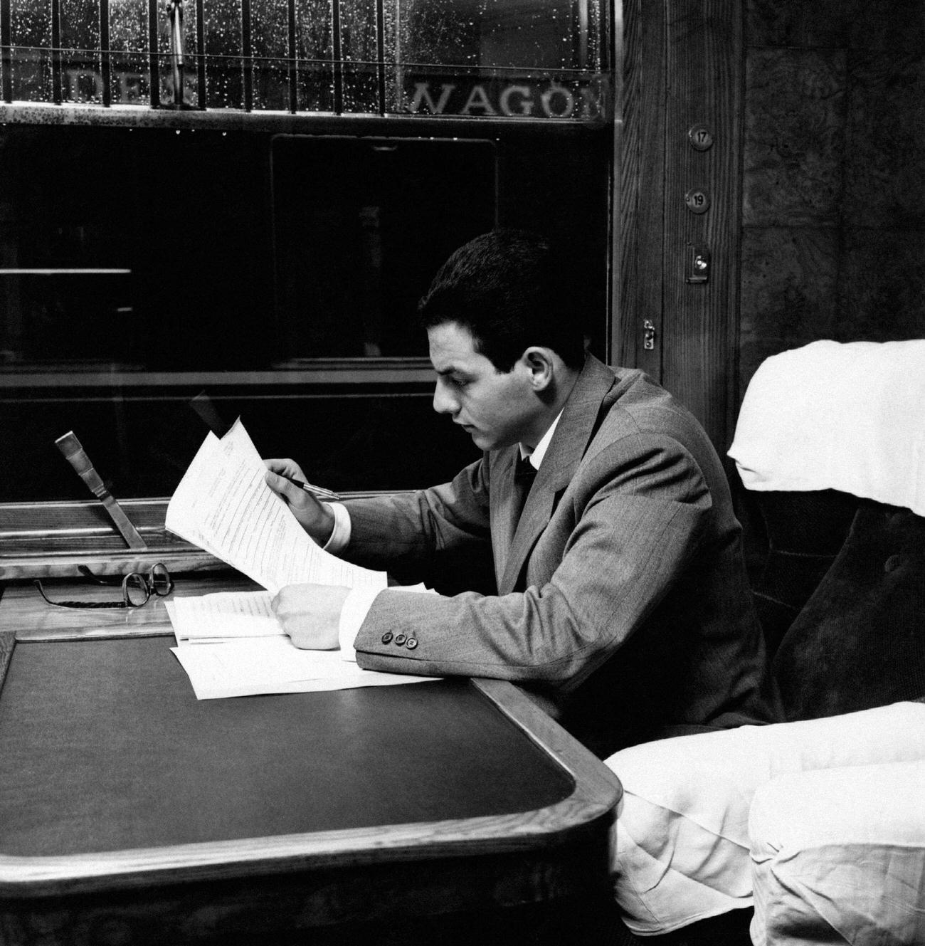 A man reading some documents on board a train. May 1963.