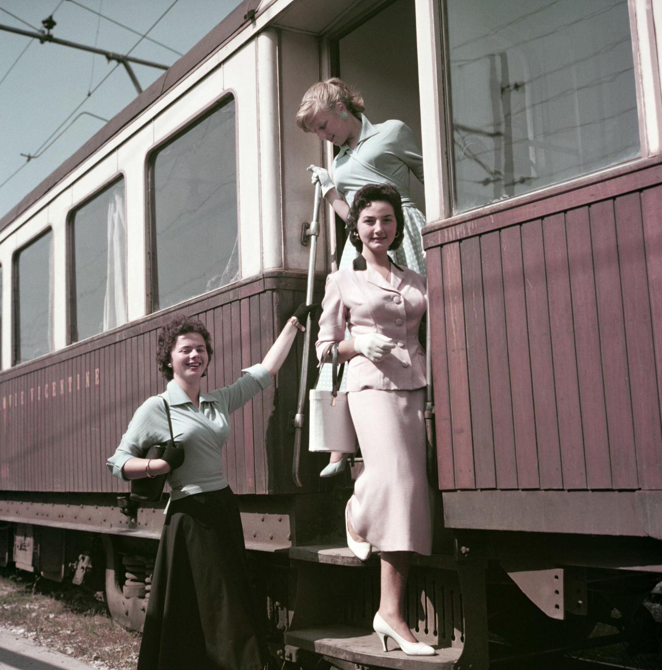 Three women getting off the train at the station. Italy, 1955
