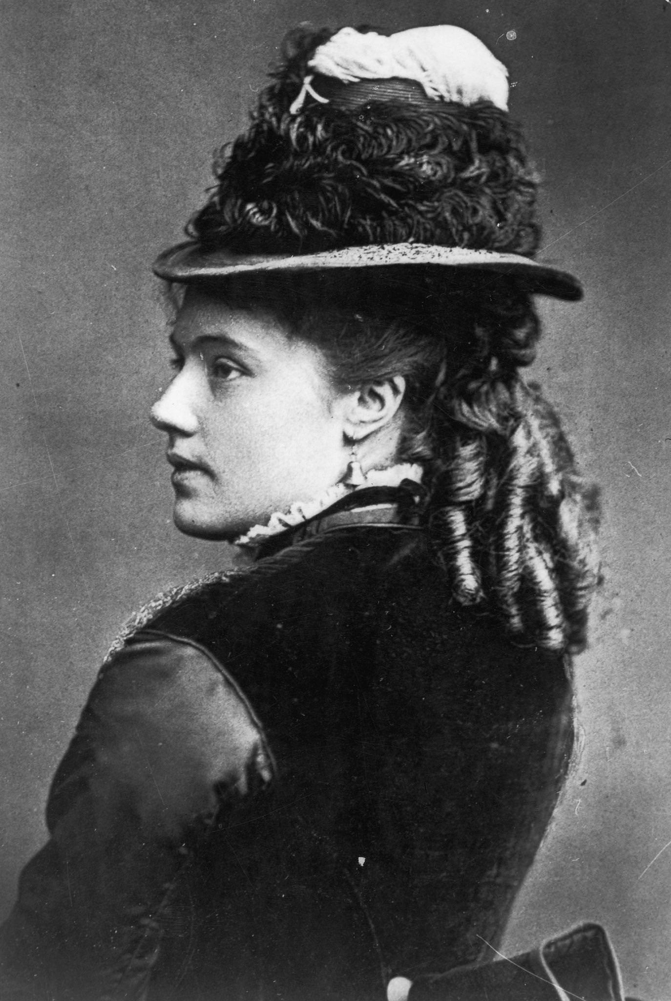A young woman with her hair in ringlets and wearing bell-shaped earrings and a hat, 1855.