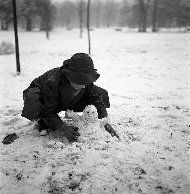 Little boy crouching and making a snowman in a park after a snowfall, Milan, 1950s. (Mario De Biasi)