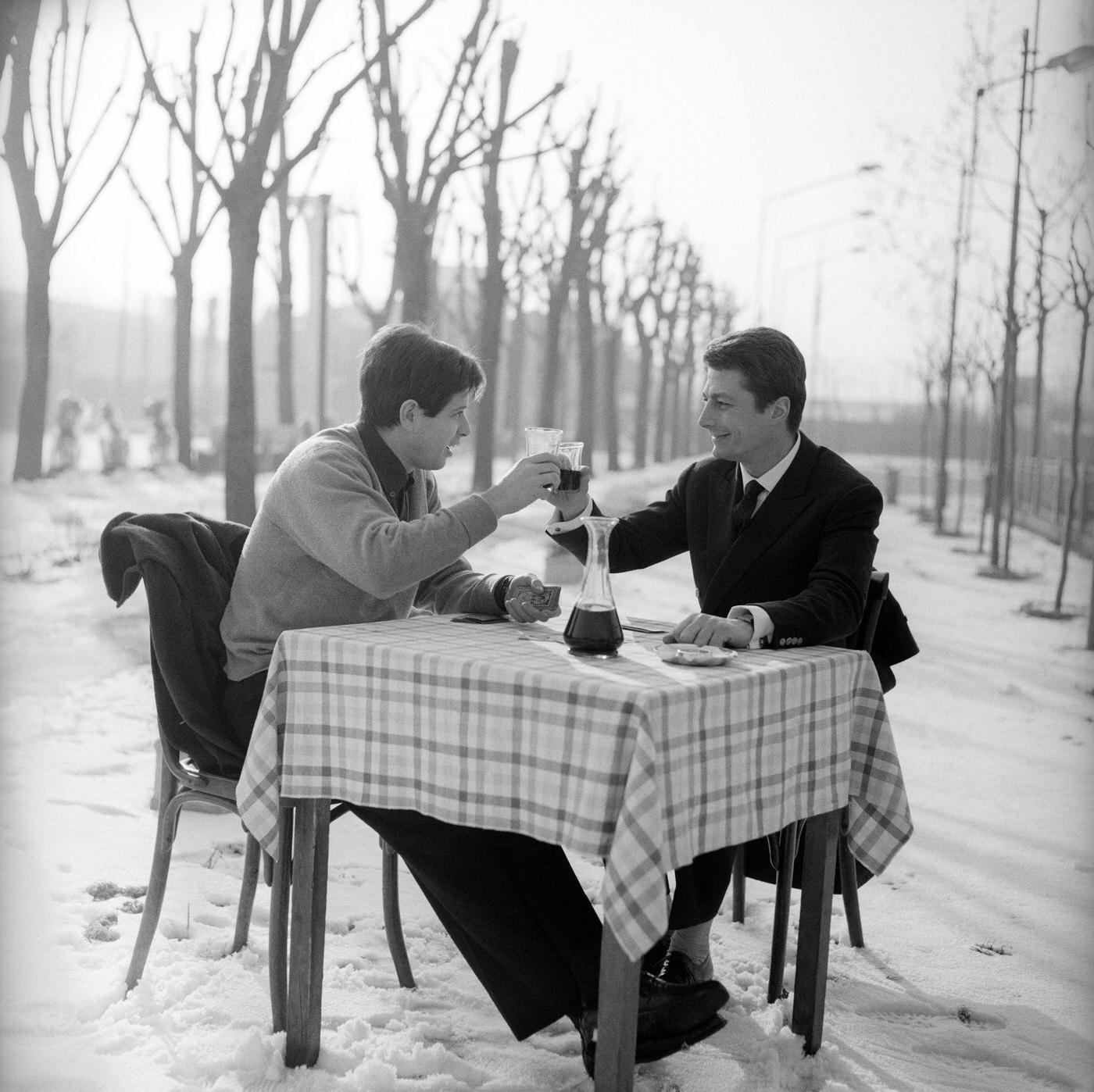 The Italian voice artist and film actor Corrado Pani and the US actor Joseph Walsh are chatting around a square table in the open air, in a snow covered landscape; they are toasting with red wine. Italy, 1963.