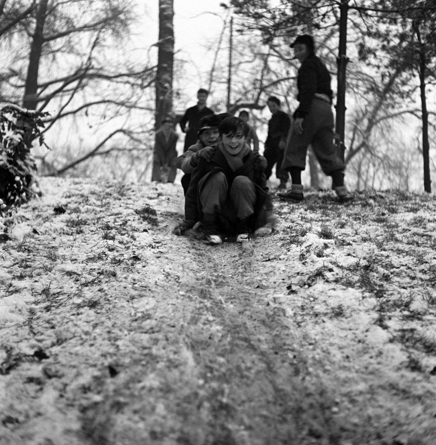 Children playing on a slope covered with snow in a park after a snowfall. Milan, 1950s.