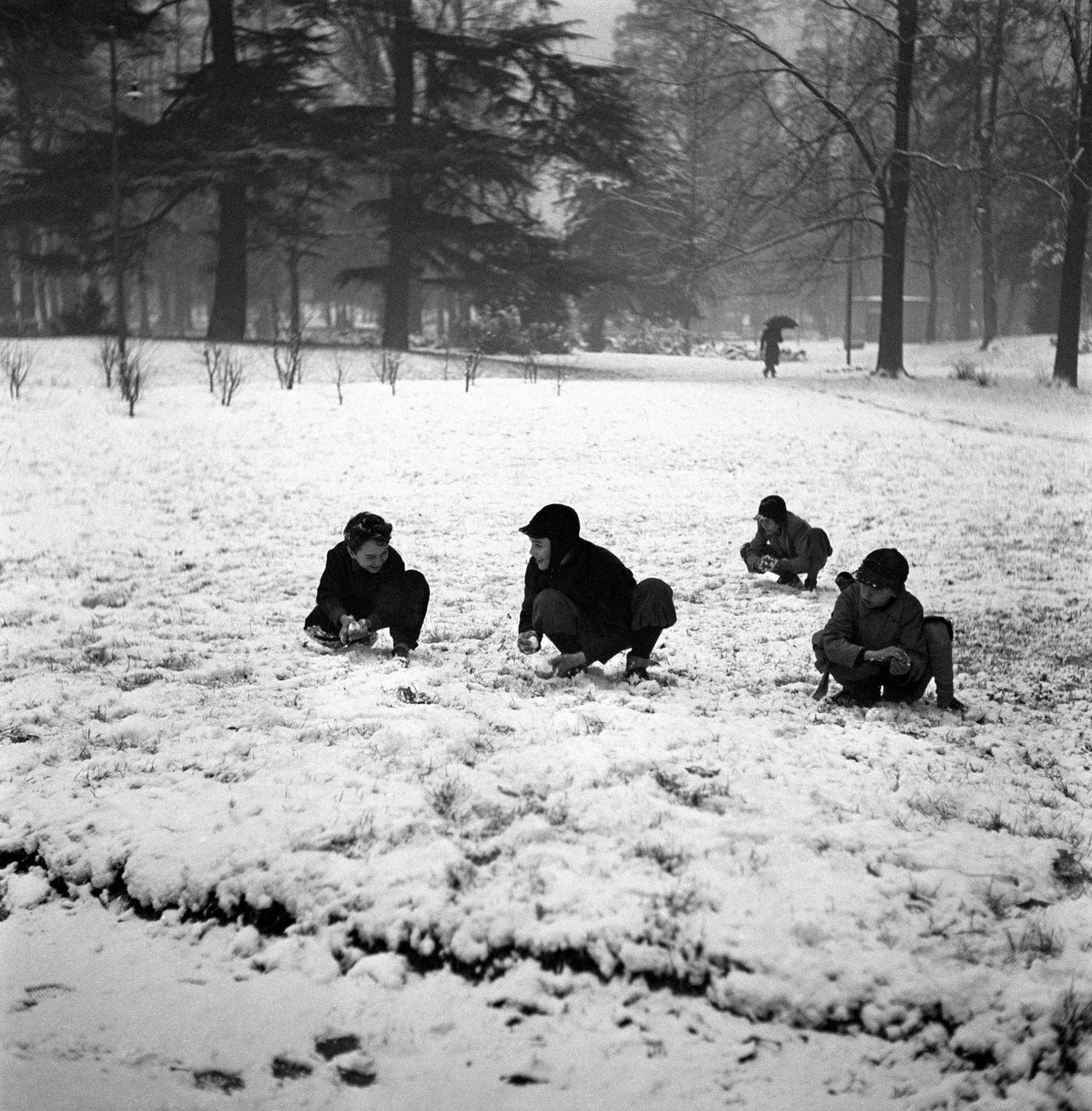 Children playing with snow in a park after a snowfall. Milan, 1950s.