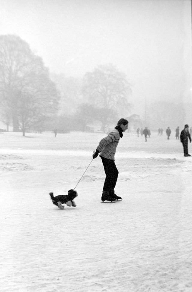 A man and his dog ice skating on a frozen lake near London, 1963.