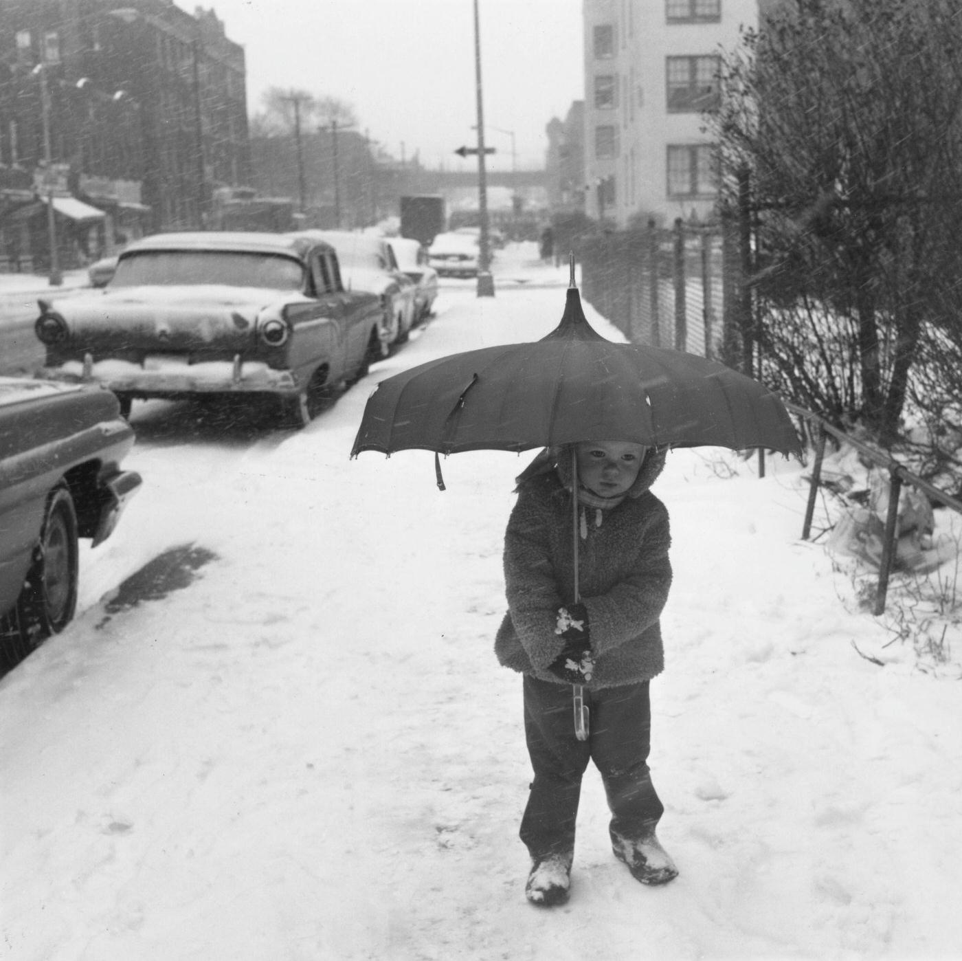 Two-year-old Mary Olskey carries an umbrella as she takes tentative steps on the snow in the Astoria neighbourhood of the Queens borough of New York City, New York, 11th February 1964