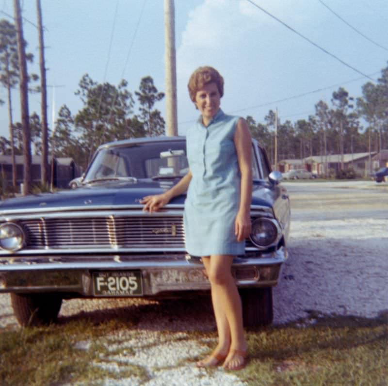 A cheerful lady in posing with a 1964 Ford Galaxie in an exotic location. The car appears to be registered in the Out Islands of the Bahamas, 1964