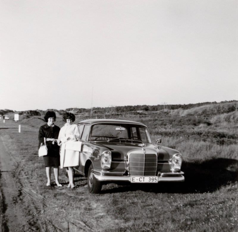 Two stylish ladies, possibly sisters, posing with a Mercedes-Benz 220 S in the countryside. The car is registered in the West German city of Essen, 1965