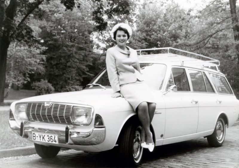 A brunette lady posing on the fender of a Ford Taunus 20M Turnier in a cobbled street. The print is dated "14.6.1966" on the reverse side. The car is equipped with a roof rack and registered in West Berlin, June 14, 1966