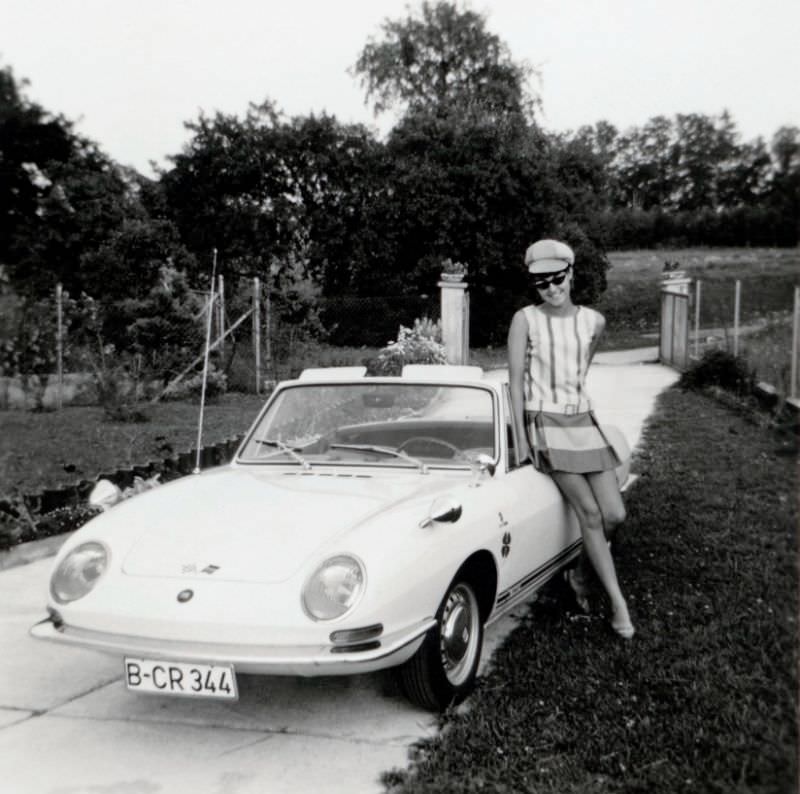 A fashionable young lady posing with a Fiat 850 Spider in the drive of a private home in summertime. The car is registered in West Berlin, 1968