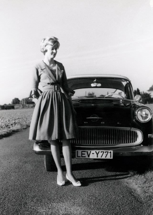 A blonde lady posing with an Opel Rekord P1 in the countryside. The car is registered in the West German town of Leverkusen, 1960s