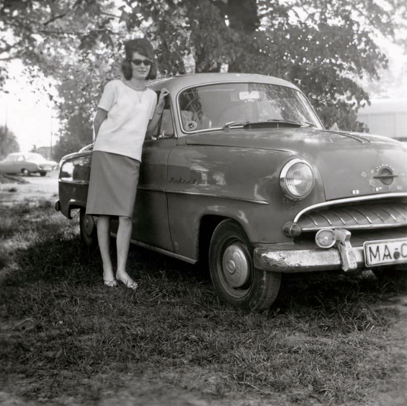 A lady with a beehive hairdo posing with a Opel Olympia Rekord on the outskirts of town. The car is registered in the West German city of Mannheim, 1960s