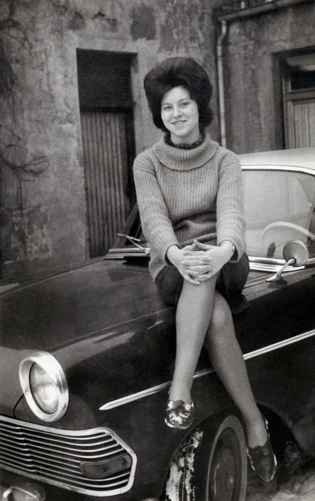 A cheerful young lady posing on the fender of an Opel Rekord P2 on a snowy winter's day, circa 1962