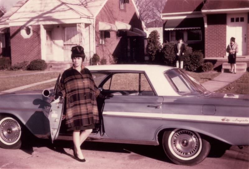 A young lady with a beehive hairdo and a checkered cape posing with a 1961 Chevrolet Impala Sport Sedan, 1962