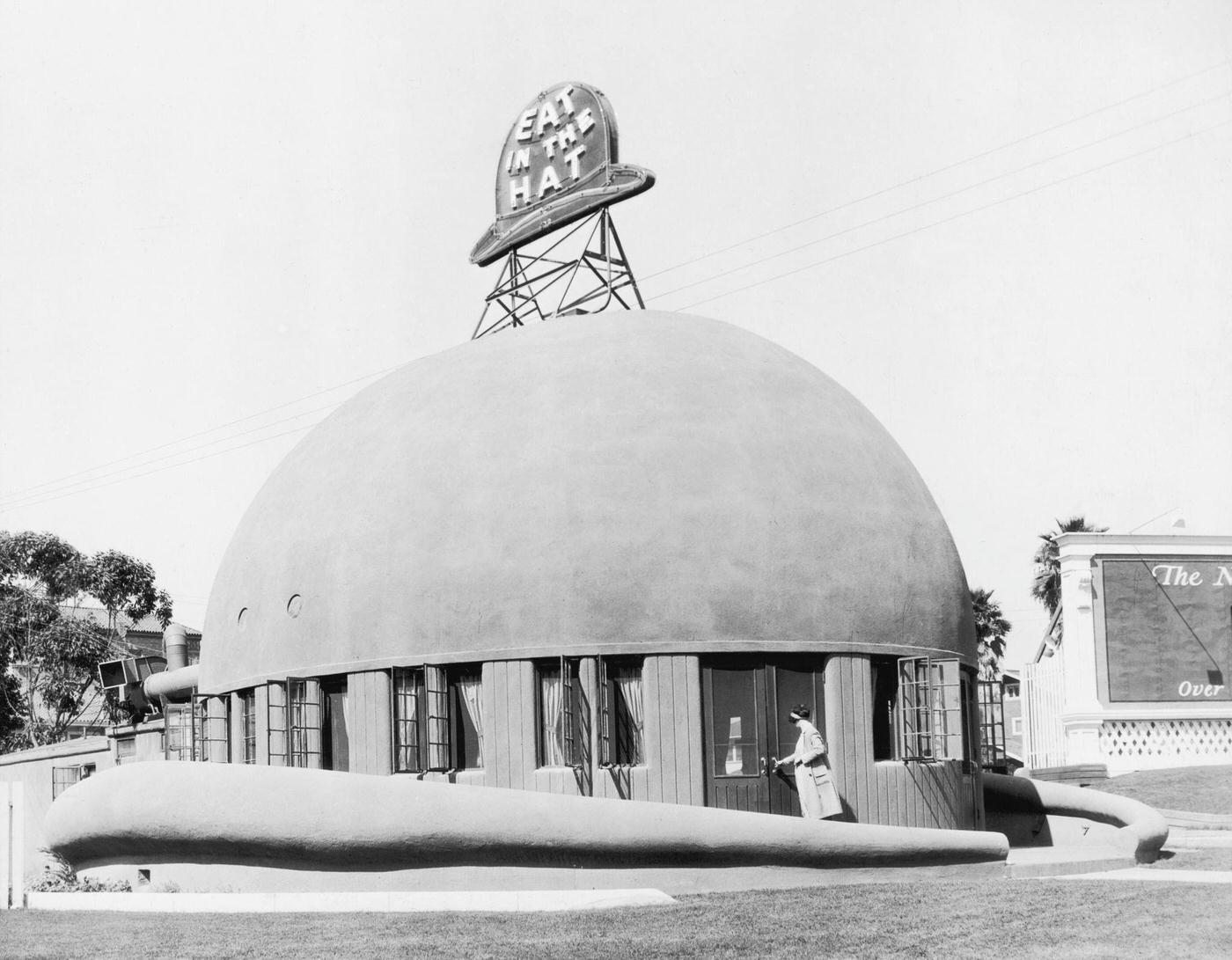 Exterior view of a woman entering the hat-shaped Brown Derby restaurant on Wilshire Boulevard, opposite the Ambassador Hotel in Hollywood, California, 1930