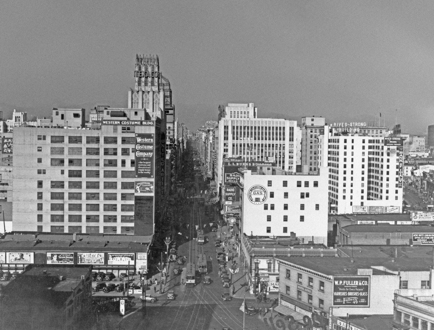 High angle view looking north on Broadway from 11th Street, with the Western Costume Building on the left, with a Texaco sign beyond that, 1930