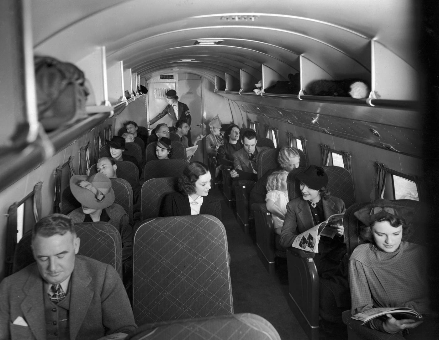 Passengers sitting in their seats inside the cabin of a 21-passenger airplane making daily trips between New York City and Chicago. Several women read magazines.