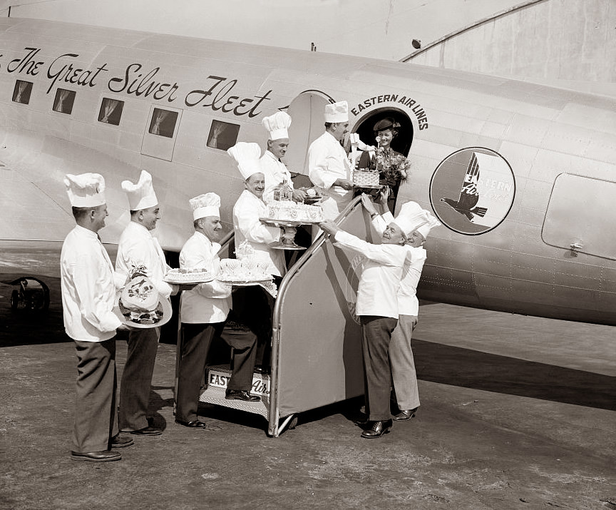 This picture is from 1938, and famous chefs are shown loading cakes onto the airplane for the passengers