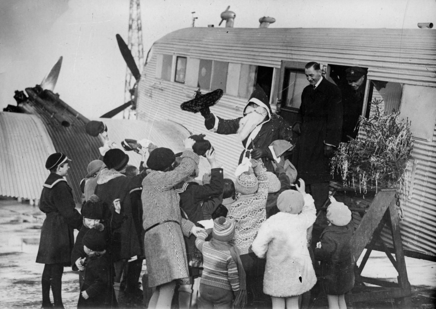 Children welcome Santa Claus as he disembarks his plane in a photograph from around 1930.