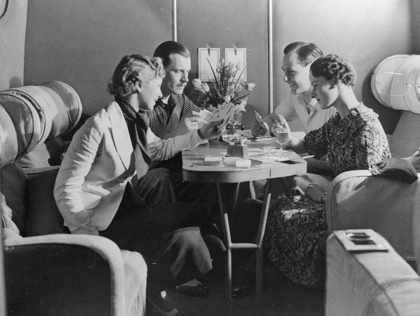 Passengers on an Imperial Airways flight enjoy a drink and a game of cards in the cabin in 1936.