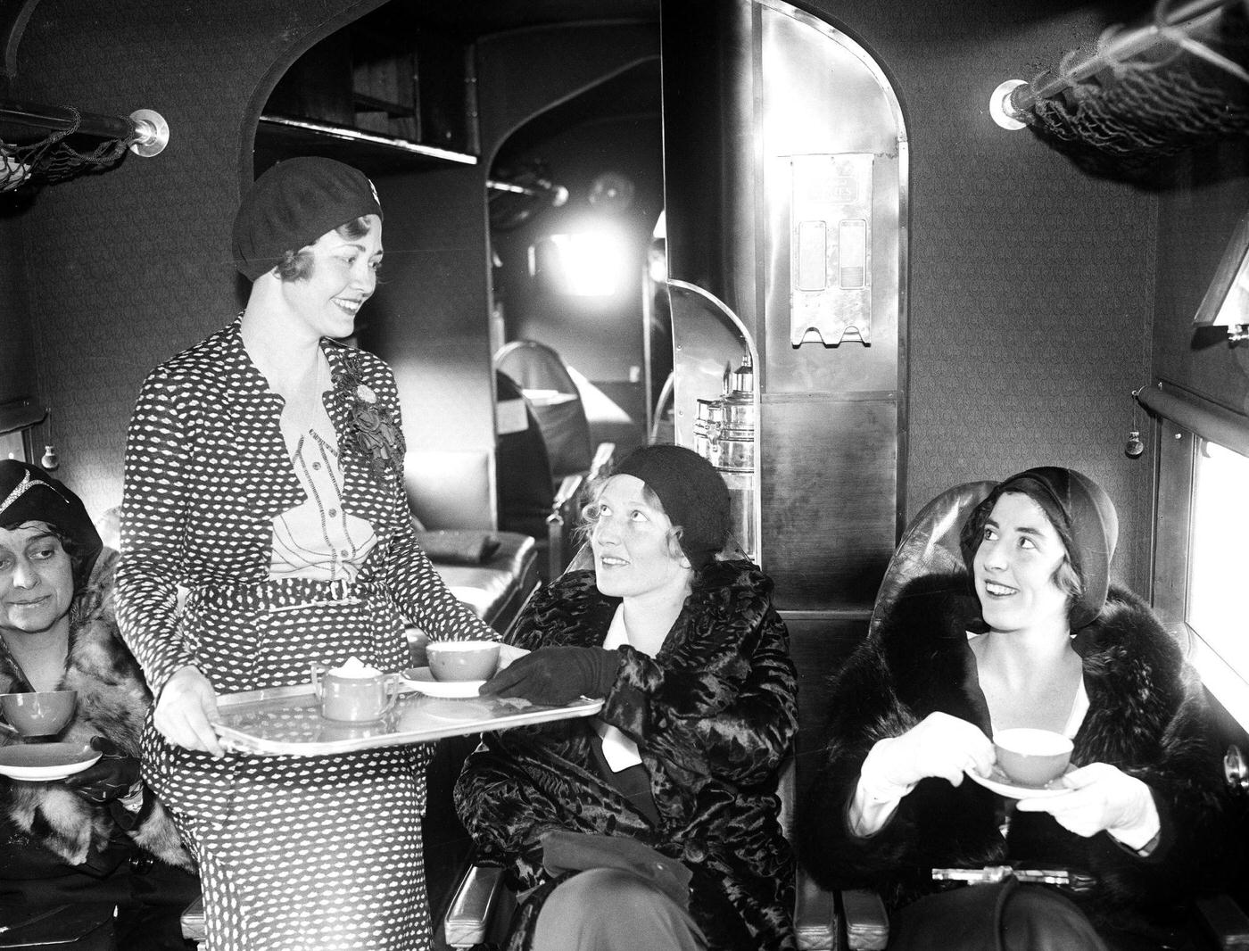Miss Wanda Wood, hostess for Eastern Air Transport, serves tea for two, Misses Charlotte Childress and Elizabeth Hume, aboard one of the line's passenger planes 1930.