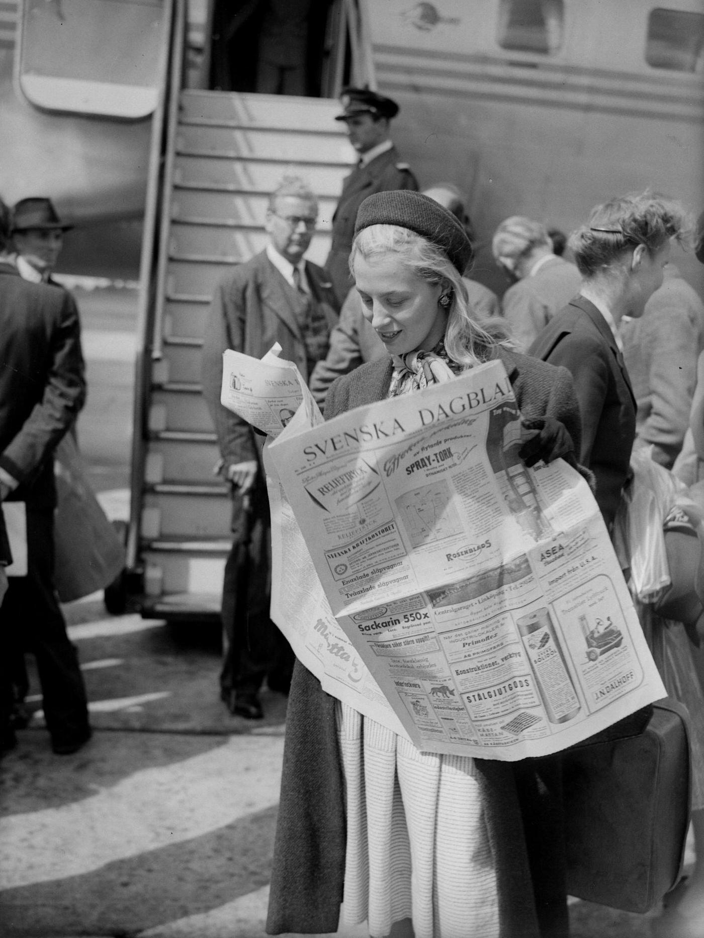 Swedish film actress Mai Zetterling is pictured reading a newspaper brought over from Sweden on the first passenger plane to arrive at Northolt Airport, England, since the merging of the Swedish, Norwegian, and Danish airlines.