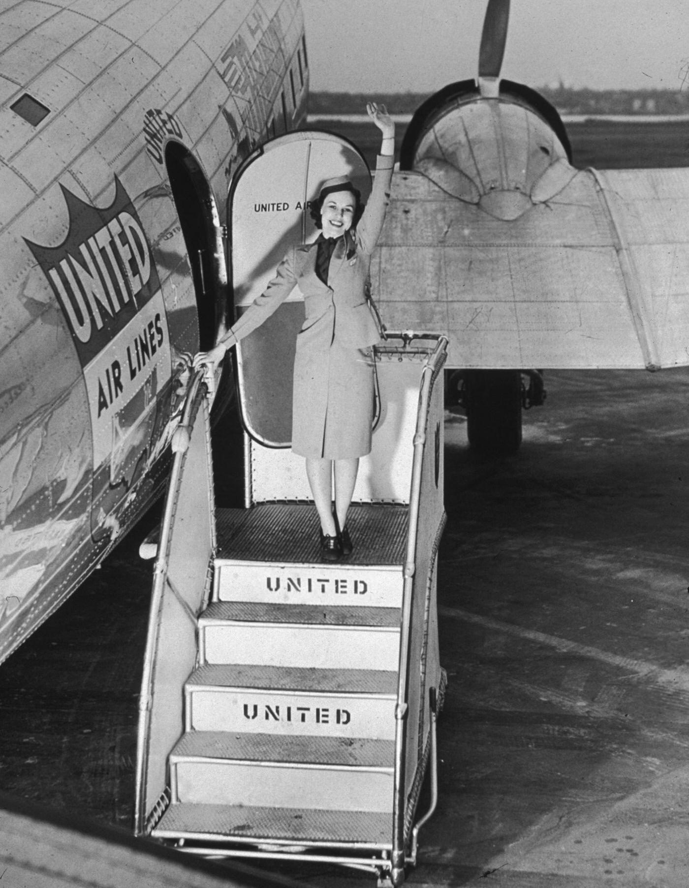 In 1945, a female flight attendant is standing on the stairway of a United Airlines airplane, waving.