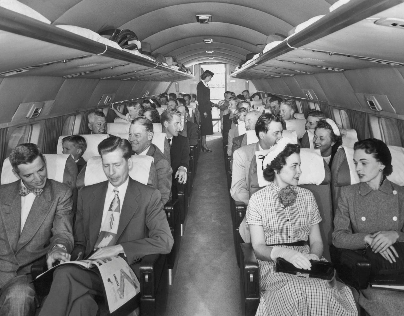 Passengers are shown seated two to a row, talking with their inflight neighbors aboard a Mainliner Convair aircraft, while the flight attendant works at the back of the plane in the late 1940s.