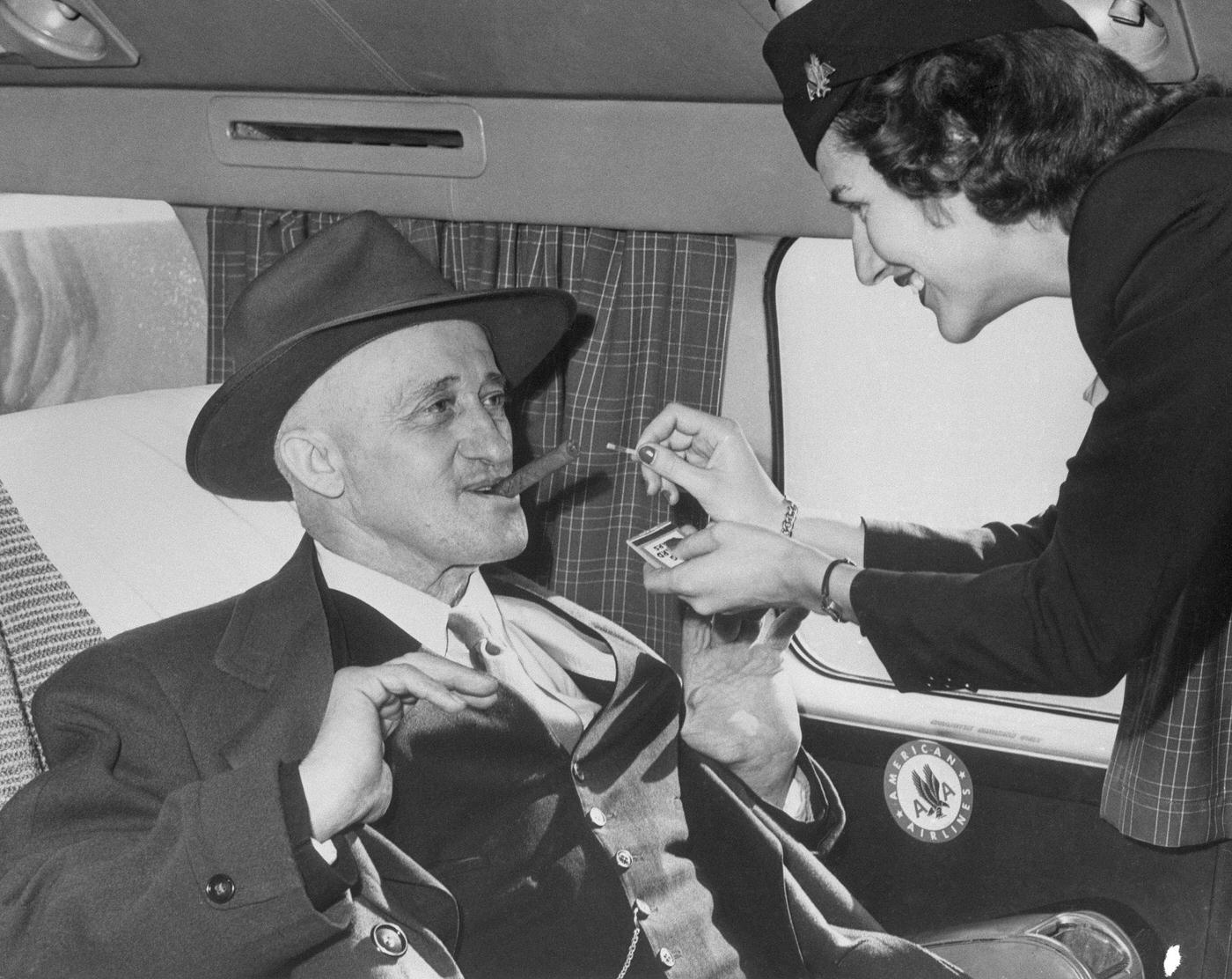 Stewardess Jane Driscoll lights a cigar for airline passenger Carl Graulein, 68, of East St. Louis, as he prepares to depart for his native Germany aboard an American Airlines overseas flight.
