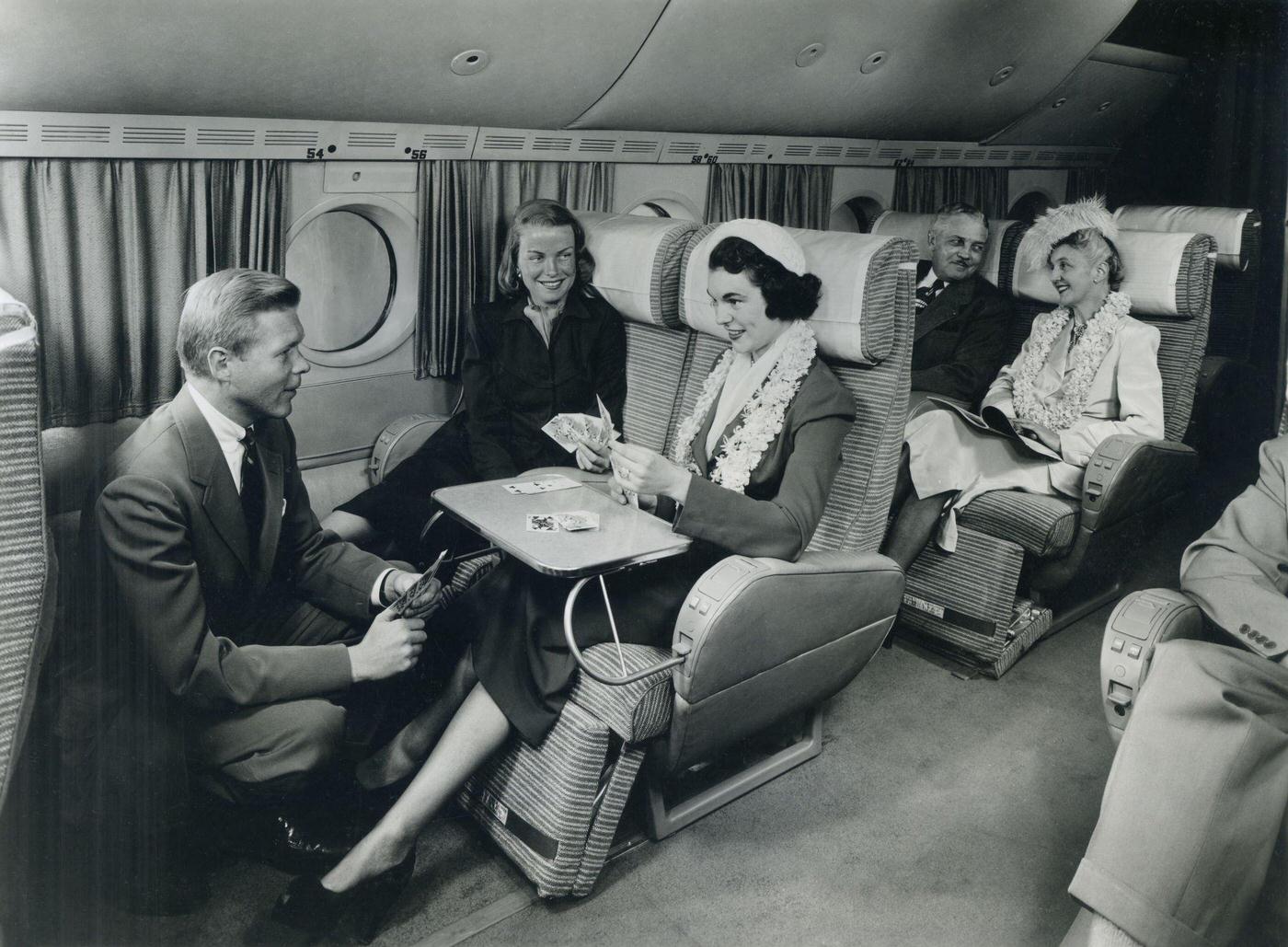 In 1949, in-flight passengers are shown playing cards and making conversation on a spacious airliner.