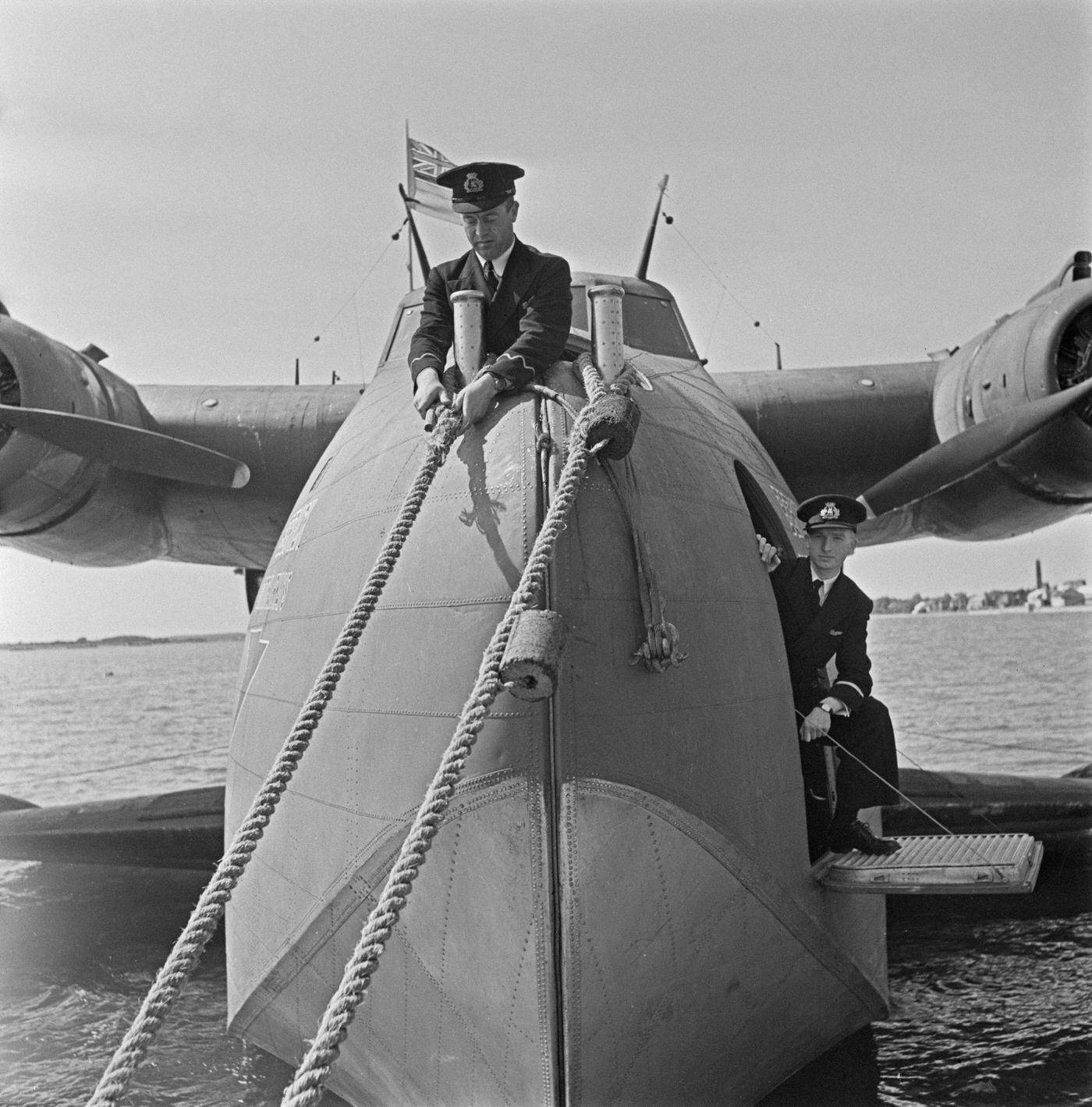 In 1942, two members of the cabin crew are casting off the mooring ropes from the British Overseas Airways Corporation (BOAC) Boeing 314A Clipper flying boat Berwick (registration G-AGCA) prior to an international flight from England.