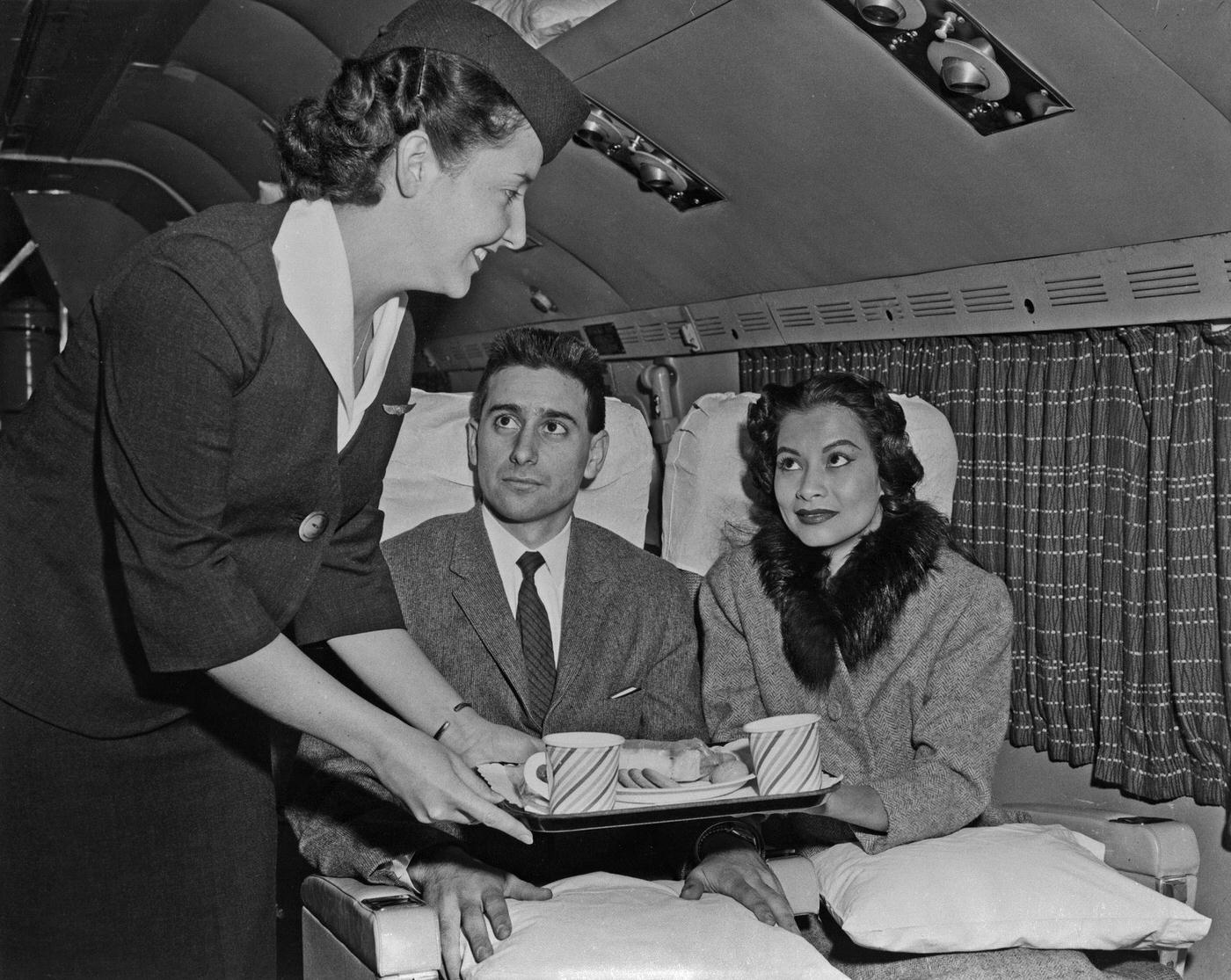In the mid-1950s, an air hostess serves a snack to passengers on a Transocean Air lines Boeing 377 Stratocruiser. Transocean Air lines was a pioneer discount airline that flew between 1946 and 1962.