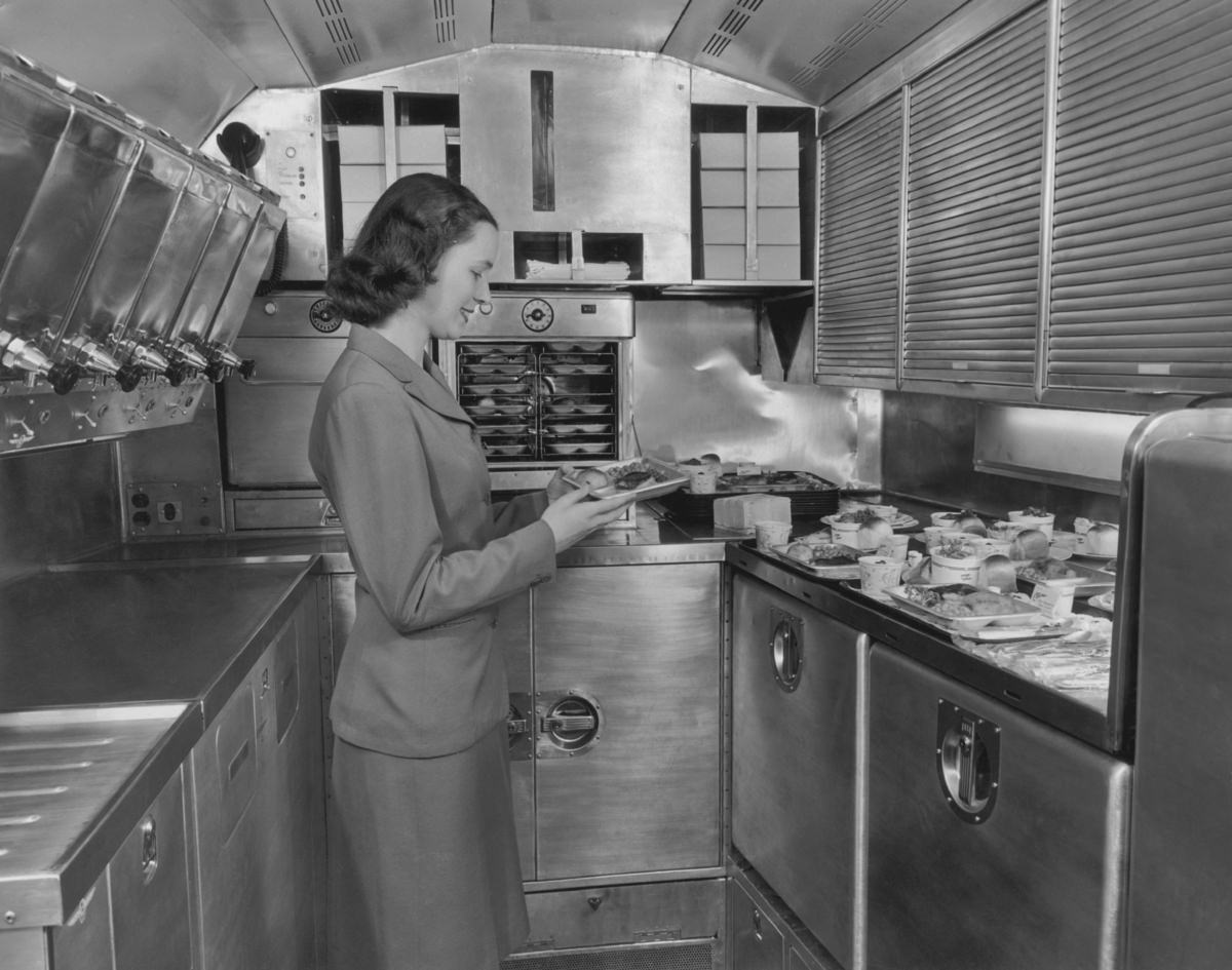 A Pan American World Airways flight attendant preparing in-flight meals in the galley of an airliner, 1950s